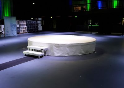 Een podium gemaakt met ronde podiumelementen. Aangevuld met wit doek en een trappetje.